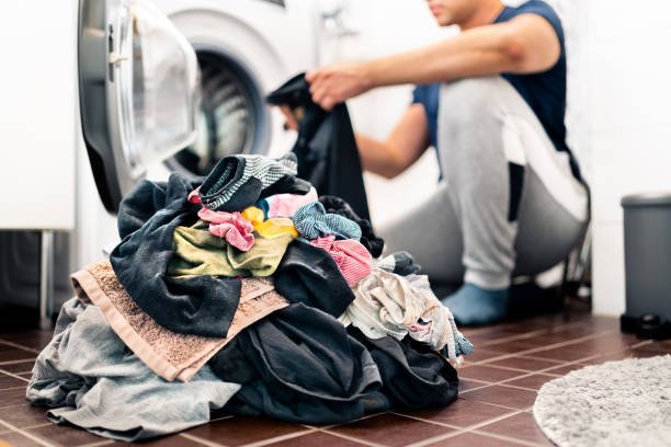 Laundry, washing clothes. Man loading washer machine and sorting by color and fabric.  Male homemaker doing house chores. Domestic work in family. Young dad and parent putting clothing in dryer.